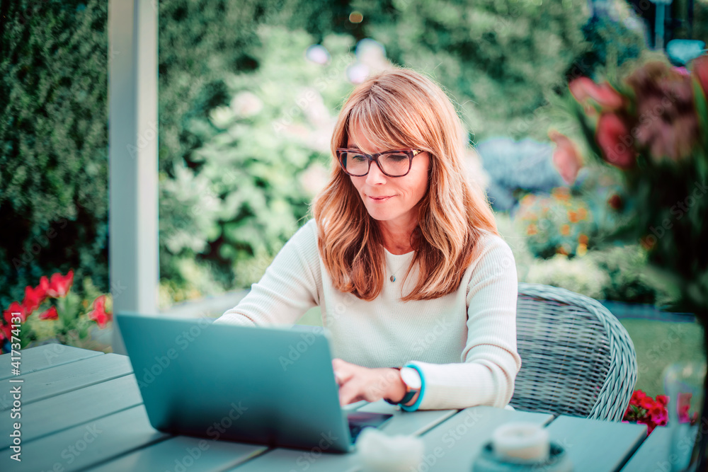 Confident woman using her laptop while sitting at balcony and working from home