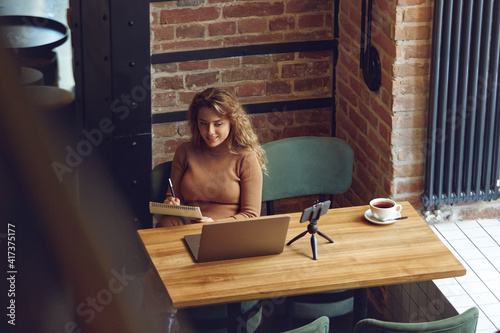 Positive woman sitting at cafe with laptop and smartphone