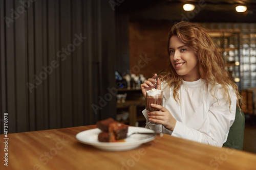 Pleasant woman relaxing at cafe with cocoa and dessert
