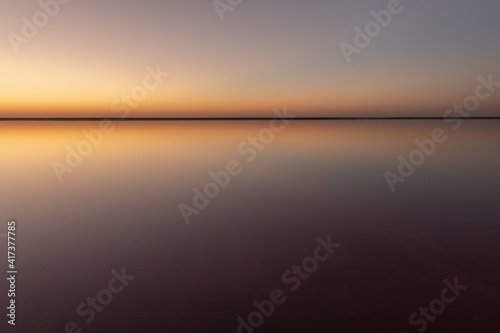 Tranquil minimalist landscape with smooth surface of the pink salt lake with calm water with horizon with clear sky in sunset time. Simple beautiful natural calm background