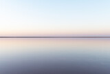 Tranquil minimalist landscape with smooth surface of the pink salt lake with calm water with horizon with clear sky in sunrise time. Simple beautiful natural calm background
