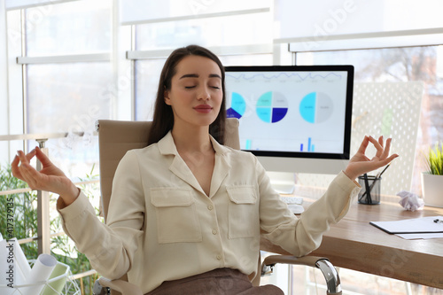 Businesswoman meditating at workplace in office. Stress relieving exercise