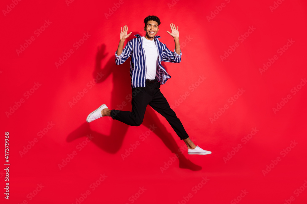 Full size photo of young cheerful afro man happy smile jump up wave hi isolated over red color background