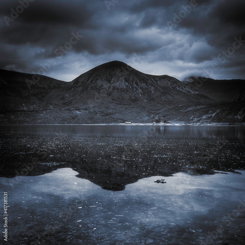 Dramatic sky over Beinn Bhreac reflecting in Loch na Dal on the Isle of Skye.The rough landscape of Scotland on a gloomy day.Dark nature photo with atmospheric mood and blue tones. photo