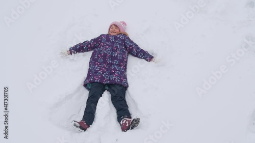 The girl lies in the snow. She makes a snow angel.