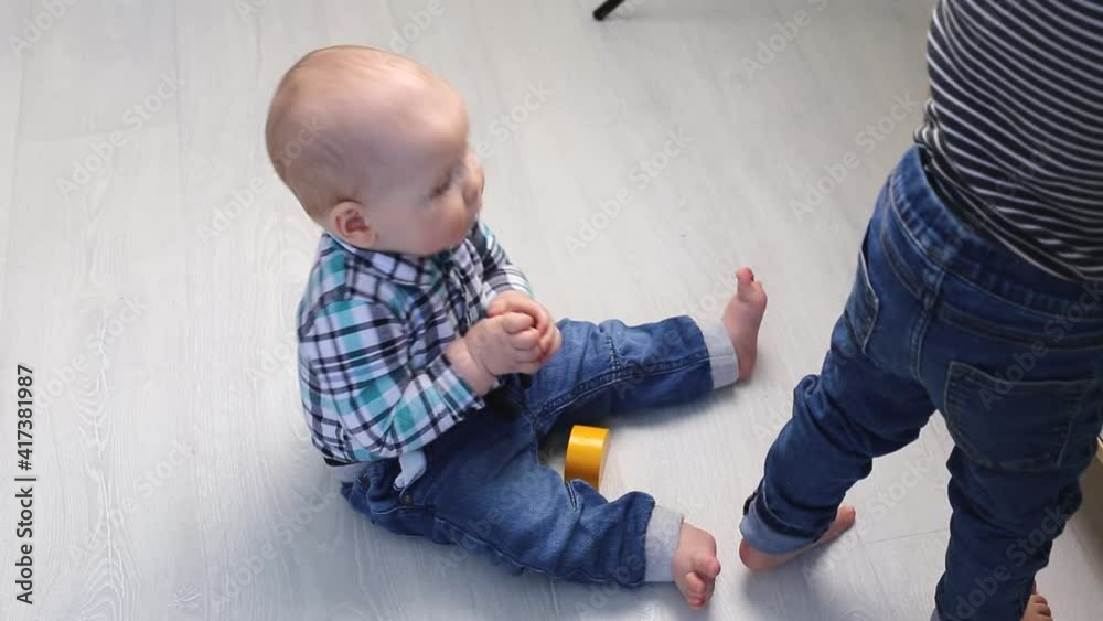 A small kid in a shirt sits on the floor of the house and licks a small toy. A small kid in a shirt sits on the floor of the house and licks a small toy.