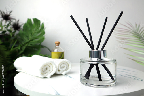 luxury aromatic scent of reed diffuser glass bottle is used as room freshener on the marble table with spa towels and masssage oil in the luxurious day spa with background of white cement wall