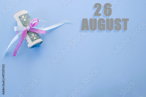 calendar date on blue background with rolled up dollar bills pinned by blue and pink ribbon with copy space. August 26 is the twenty-sixth day of the month