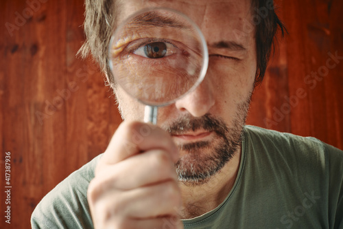 Curious man looking through magnifying glass