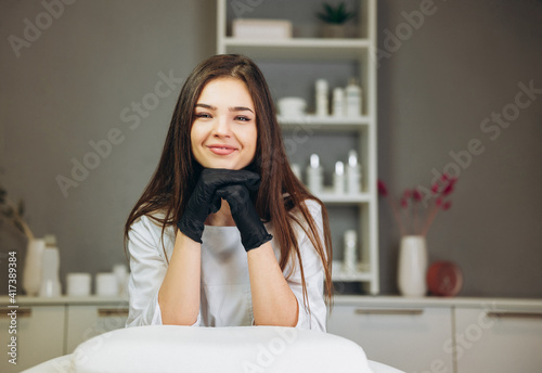 Consultation in cosmetology clinic. Female beauty doctor in white coat and black gloves smiles nicely. Healthcare concept.