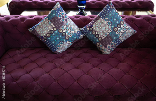 Purple velvet fabric modern sofa with sunken buttons and colorful decorative pillows.