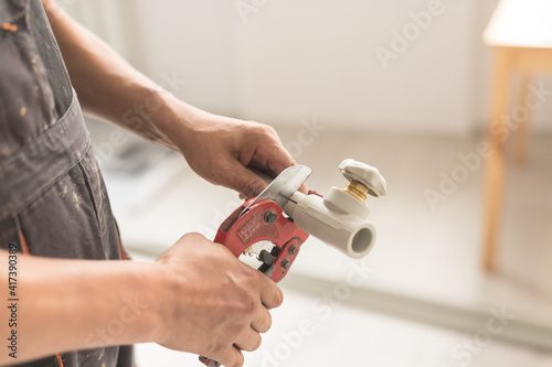 Close-up of hand with yellow scissors cut pipes for heating or water supply