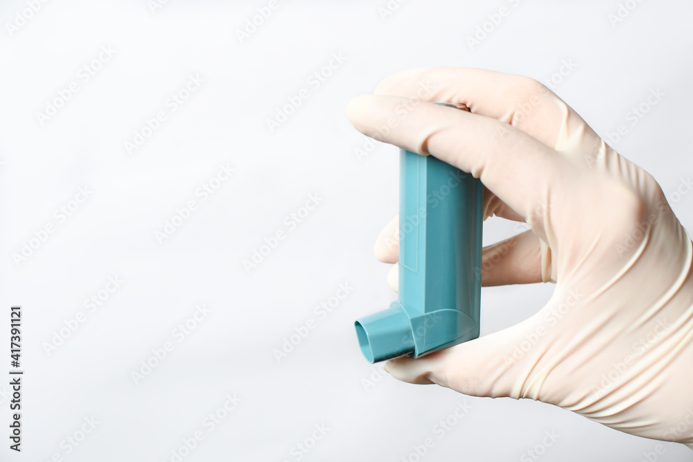 A woman's hand in a glove, the doctor's hand holds an asthma inhaler