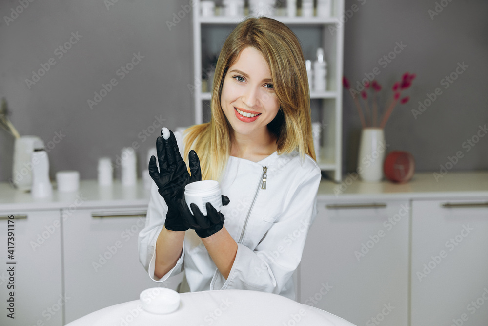 Consultation in cosmetology clinic. Female beauty doctor showing cream or mask. Healthcare concept.