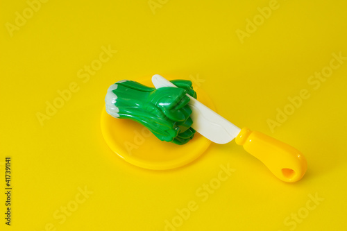 Creative composition of toy broccoli with a knife on a yellow background.