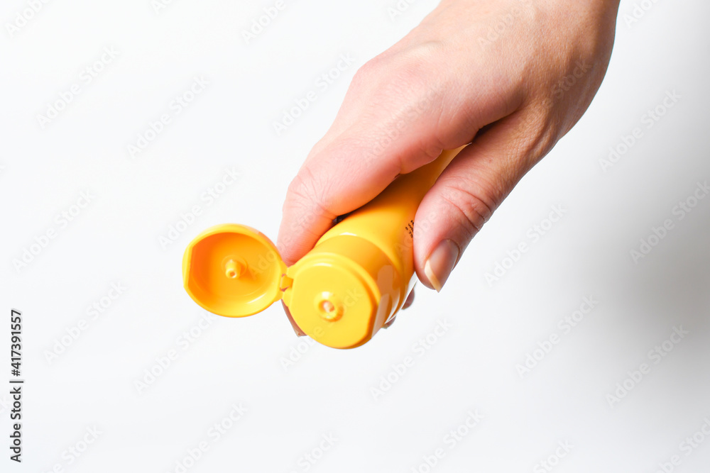 A female hand holds a yellow tube of cream on a white background.
Applying cream to the hand