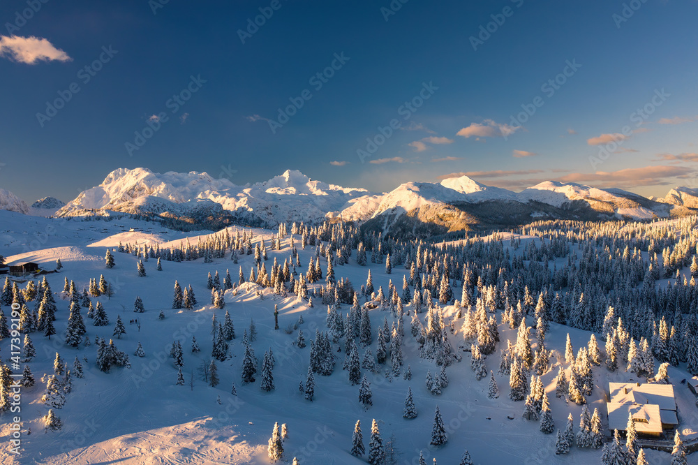 Aerial view of winter landscape with snow covered forest in the mountains with beautiful sunset light.