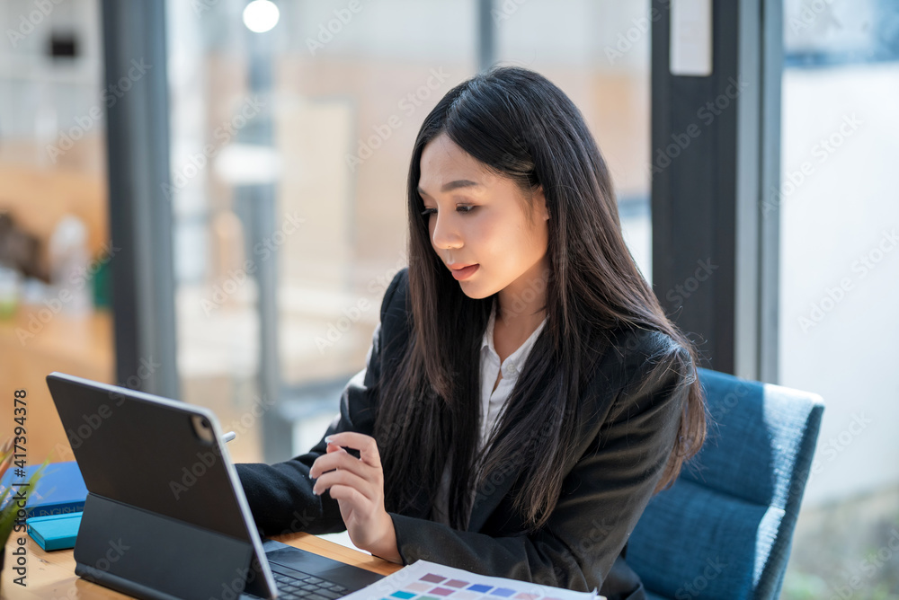 Obraz premium Asian businesswoman working on a tablet with documents at the desk in the office.