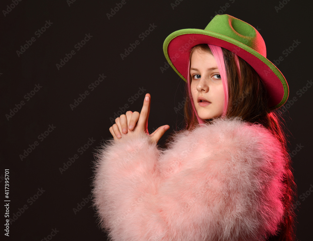 Close-up of a mysterious girl in bright clothes looks to the side and folds a gun from her fingers. Girl in a fluffy coat, hat and with strands in her hair, on a black background Close-up of a mysterious girl in bright clothes looks to the side and folds a gun from her fingers. Girl in a fluffy coat, hat and with strands in her hair, on a black background
