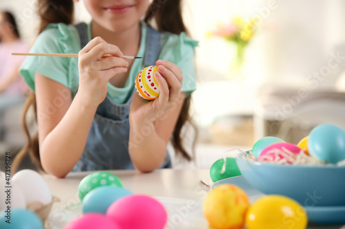Little girl painting Easter eggs at table indoors, closeup