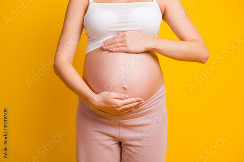 Cropped view of attractive pregnant girl touching large stomach parenthood preparation isolated over bright yellow color background © deagreez