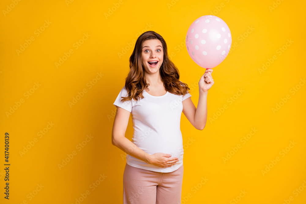 Portrait of lovely amazed cheery pregnant girl holding in hand air ball childbirth isolated over bright yellow color background Portrait of lovely amazed cheery pregnant girl holding in hand air ball childbirth isolated over bright yellow color background