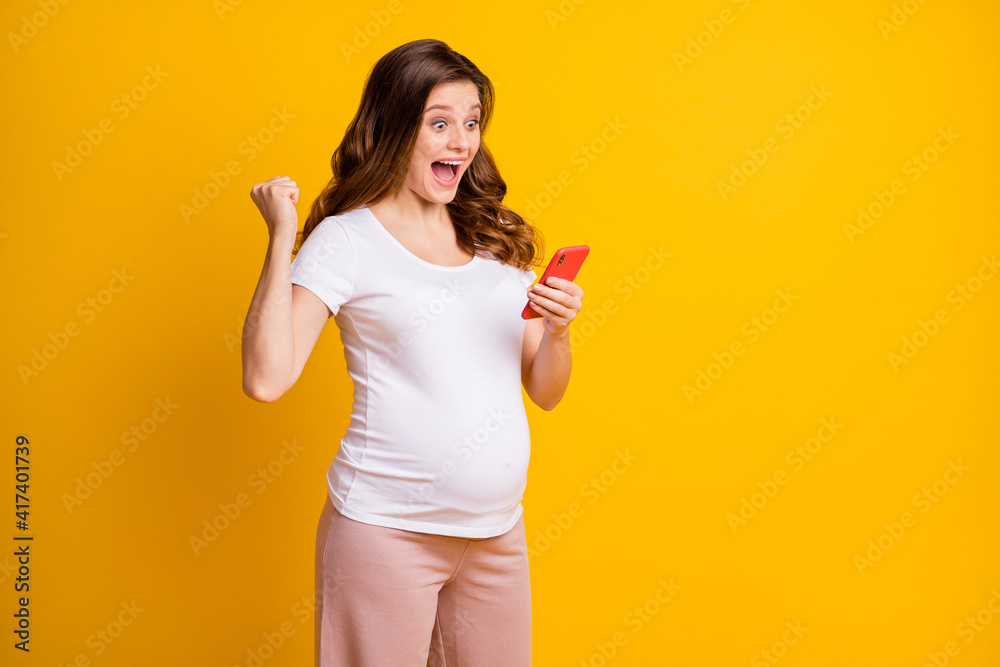 Portrait of pretty cheerful pregnant girl using device app having fun fast 5g isolated over bright yellow color background Portrait of pretty cheerful pregnant girl using device app having fun fast 5g isolated over bright yellow color background