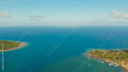 Seascape: shore of island Balabac with forest and palm trees, coral reef with turquoise water, top view. Coastline of tropical island covered with green forest against the blue sky with clouds and