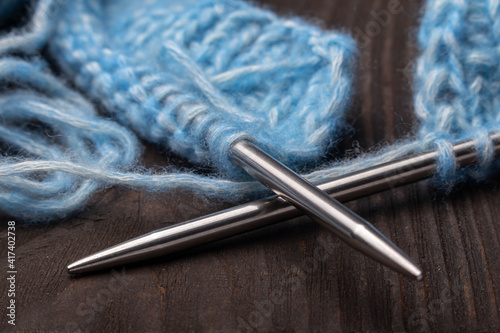 knitting needles with blue wool yarn close up on a dark wooden background