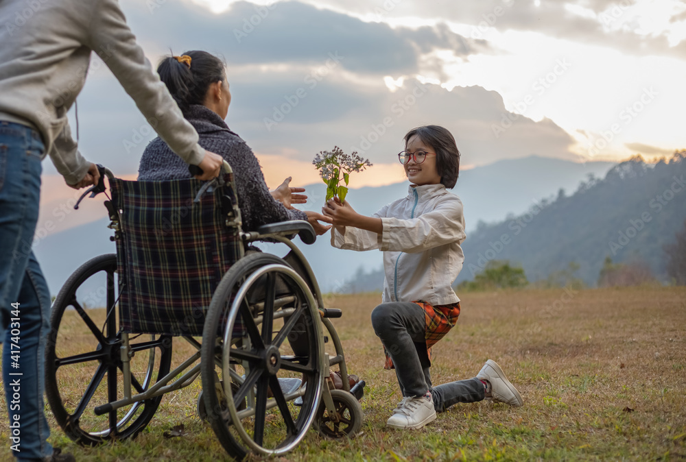 disabled handicapped woman sitting on her wheelchair with her daughter and care helper at sunset disabled handicapped woman sitting on her wheelchair with her daughter and care helper at sunset