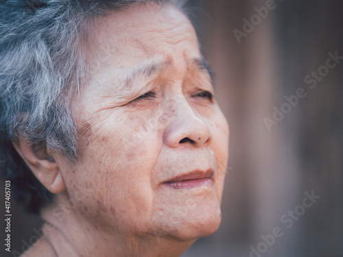 Senior woman with short gray hair, looking away and the face of worried while standing outdoors with wooden wall background. Side view. Space for text. Concept of aged people and healthcare