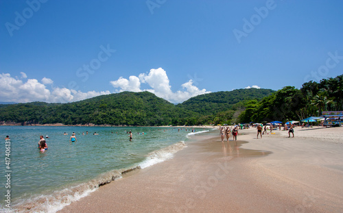 Praia brasileira de Ubatuba no litoral de São Paulo, em dia de verão com céu azul e banhistas curtindo as férias no mar. Pessoas tomando banho de sol e na água.