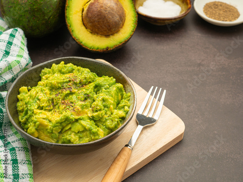 Fresh guacamole on a dish placed on a cutting wooden board with ingredients for homemade guacamole: avocados, lemon, salt, and pepper. Top view. Concept of traditional Mexican preparation