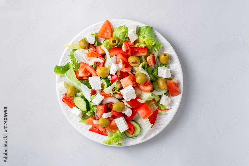 Delicious vegetable greek salad with feta, tomatoes, olives, greens on light background. Served with towel, fork and olive oil dressing. Healthy diet lunch idea. Quick, simple recipe. Delicious vegetable greek salad with feta, tomatoes, olives, greens on light background. Served with towel, fork and olive oil dressing. Healthy diet lunch idea. Quick, simple recipe.