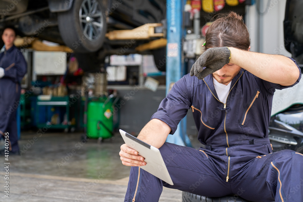 Caucasian male technician sitting with tried from hard work on car service automobile Caucasian male technician sitting with tried from hard work on car service automobile