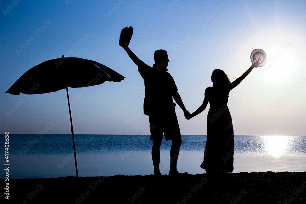 Fototapeta premium A Happy couple by the sea at sunset on travel silhouette in nature