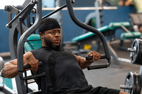 Motivated black guy having workout on chest press machine