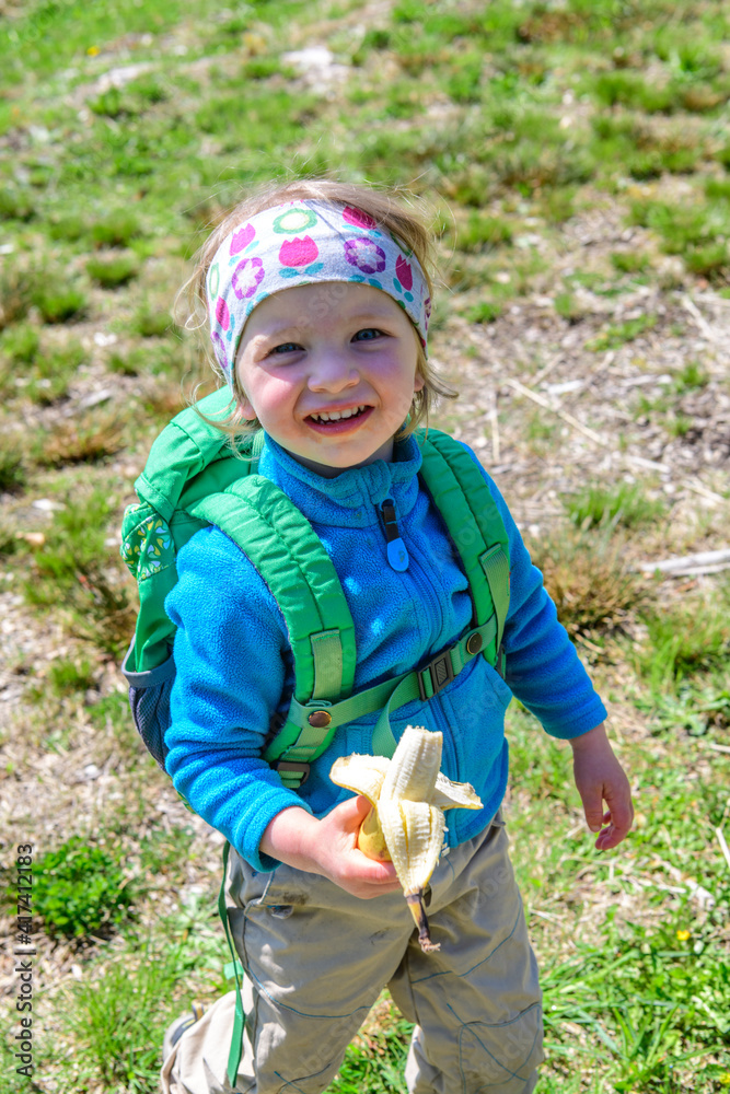 Fröhliches kleines Mädchen beim Essen einer gesunden Banane beim Wandern Fröhliches kleines Mädchen beim Essen einer gesunden Banane beim Wandern