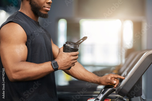 Unrecognizable sportsman with protein drink standing on treadmill