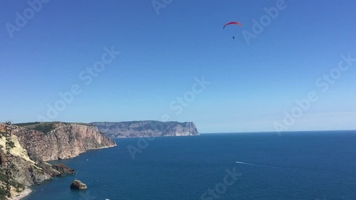 A man on a parachute glides over the sea along the mountainous coast.