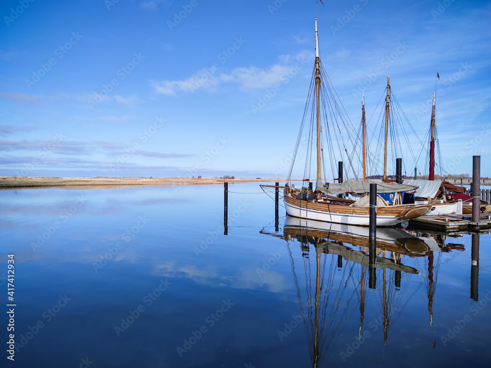 Obraz premium Photo of modern and old boats in harbor near wooden pier in calm sunset light