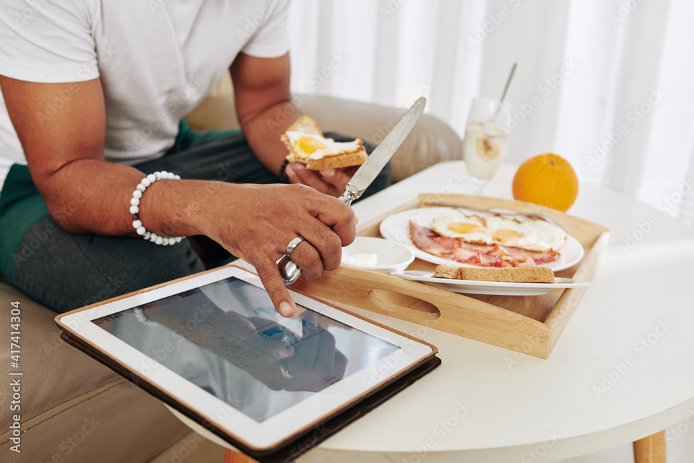 Close-up image of man eating breakfast and checking stock market data on scren of tablet computer Close-up image of man eating breakfast and checking stock market data on scren of tablet computer