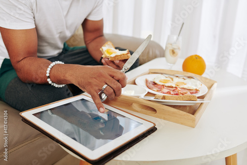 Close-up image of man eating breakfast and checking stock market data on scren of tablet computer © DragonImages