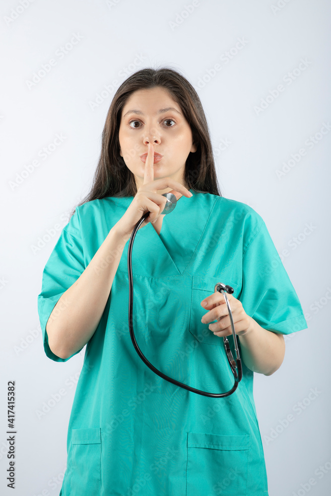 Portrait of a young woman doctor with stethoscope in uniform showing silent sign Portrait of a young woman doctor with stethoscope in uniform showing silent sign