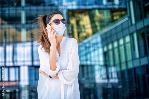 Confident woman wearing face mask while standing on the street and using mobile phone