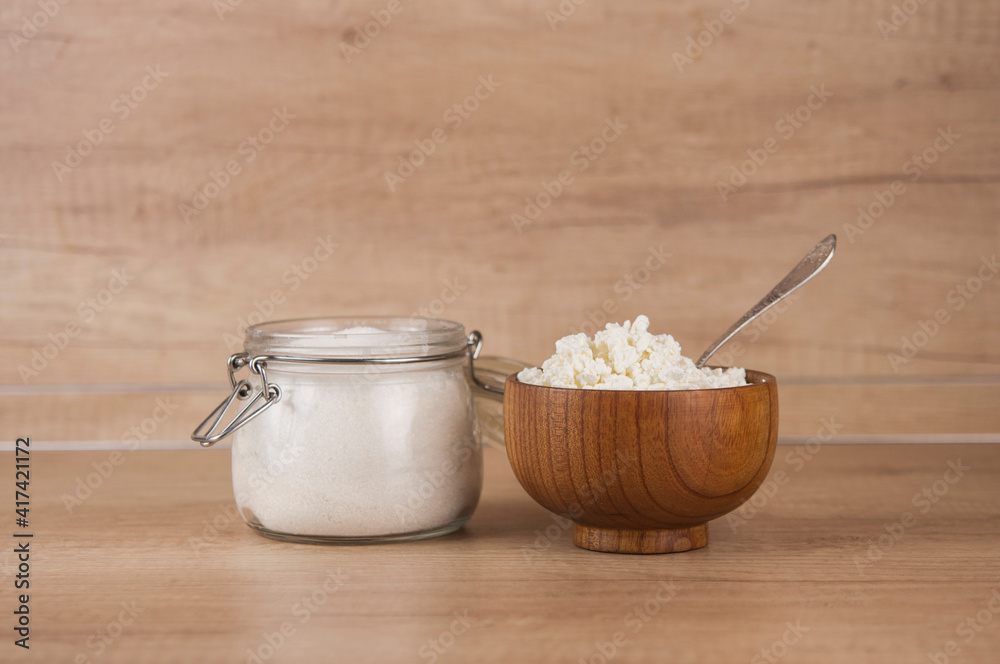 Glass jar with sugar and wooden bowl with cottage cheese on wood kitchen table Glass jar with sugar and wooden bowl with cottage cheese on wood kitchen table
