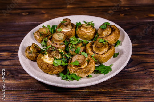 Plate with baked champignons, dill and parsley on a wooden table