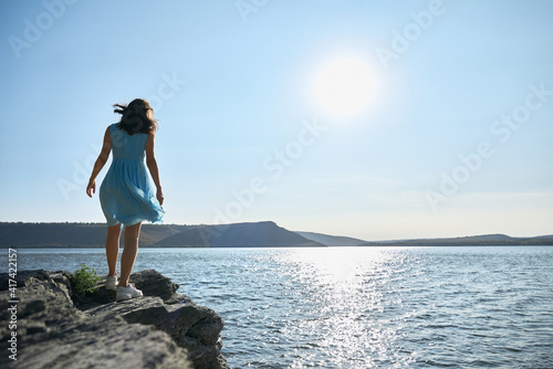 Young woman in blue dress walking along riverside