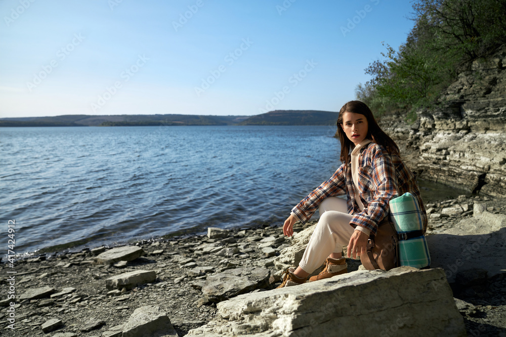 Beautiful woman with backpack sitting near Dniester river
