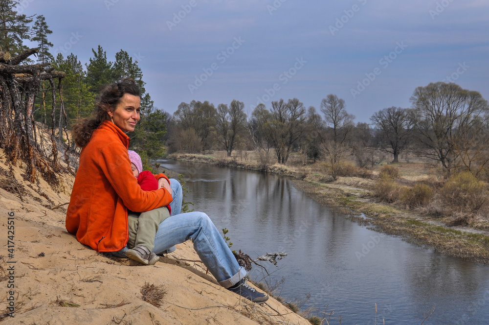 Happy mother with a child are sitting on the high bank of the Teteriv river with a beautiful panoramic view